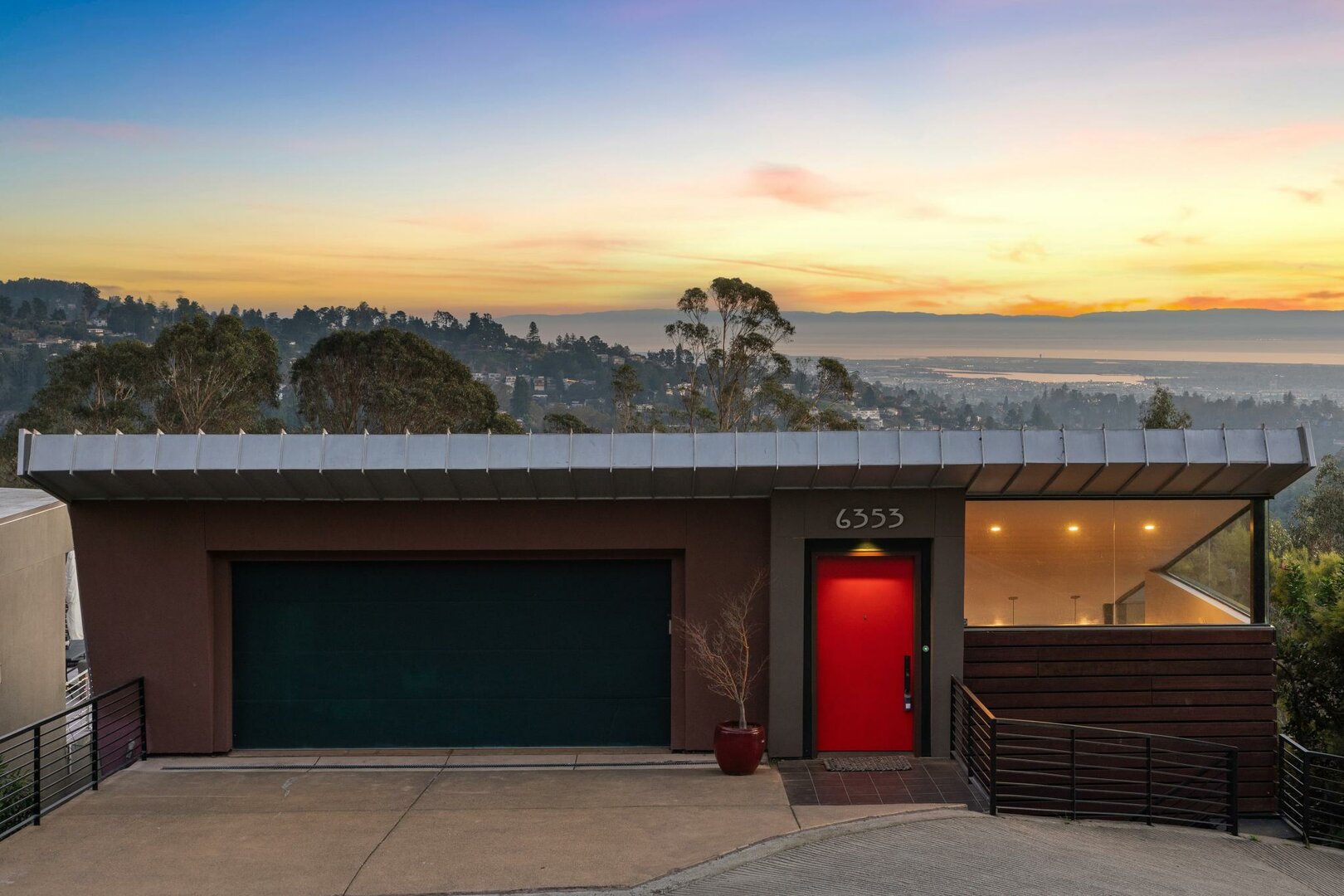 Modern hillside home facade with red front door and two-car garage at sunset