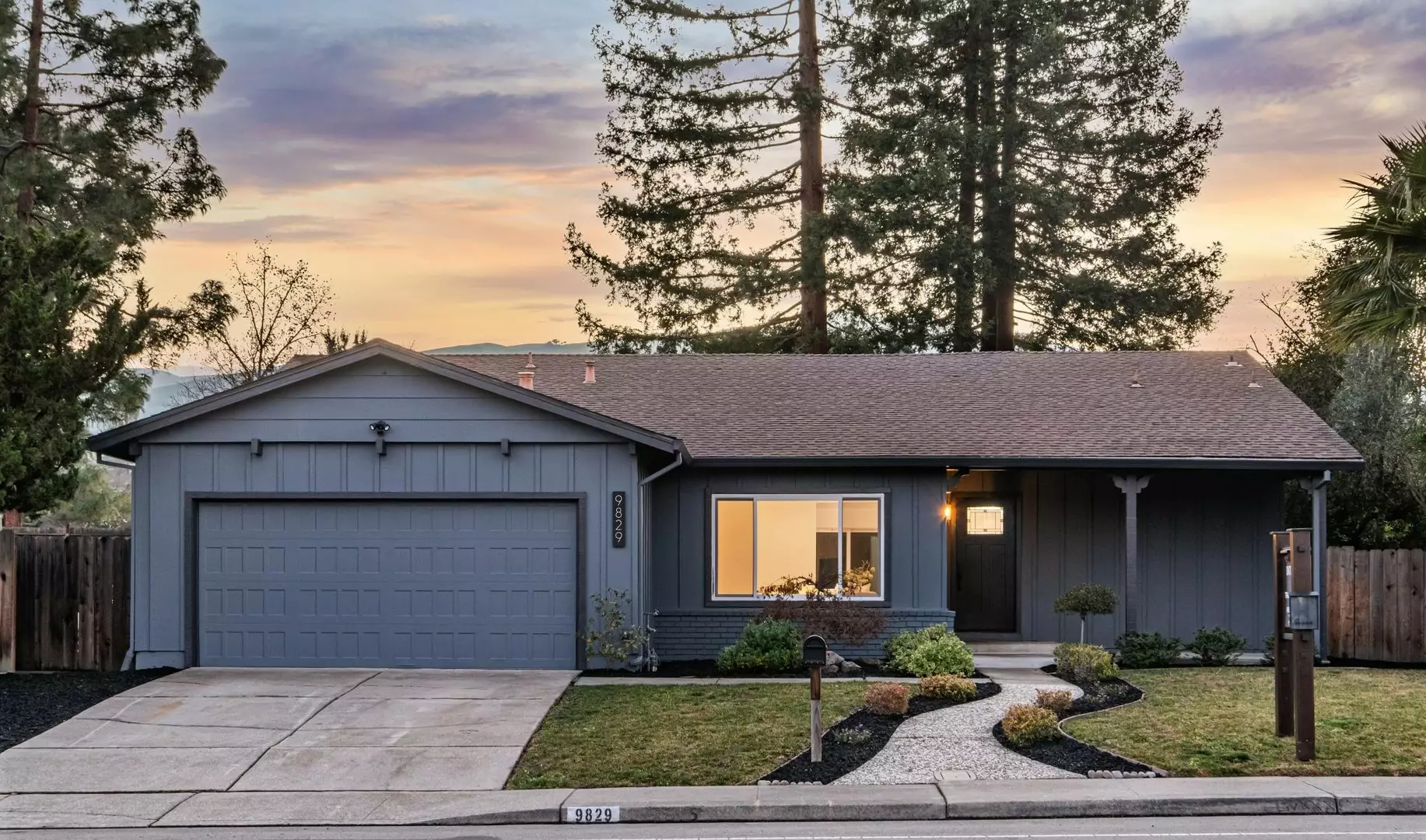 Single-story home with driveway, two-car garage and landscaped front yard at dusk