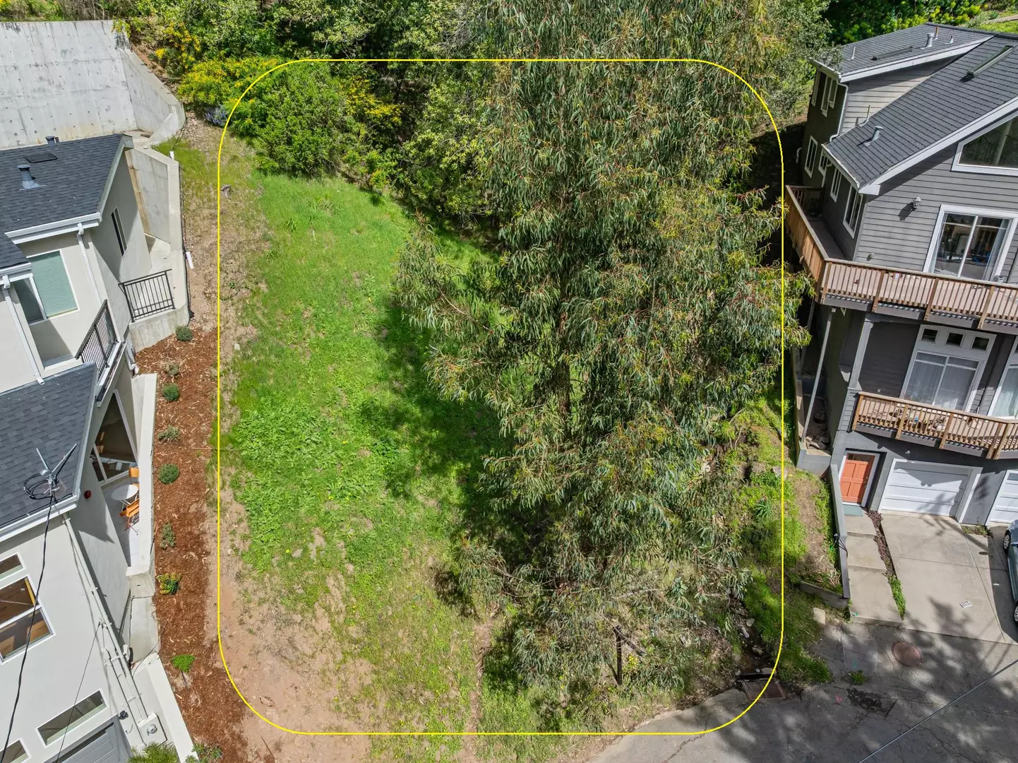 Aerial view of a grassy vacant lot with trees between houses
