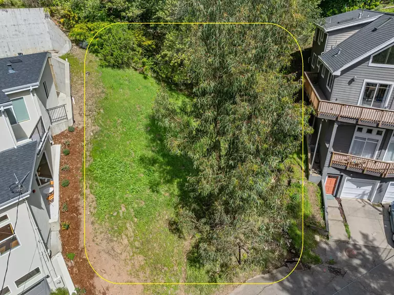 Aerial view of a grassy vacant lot with trees between houses