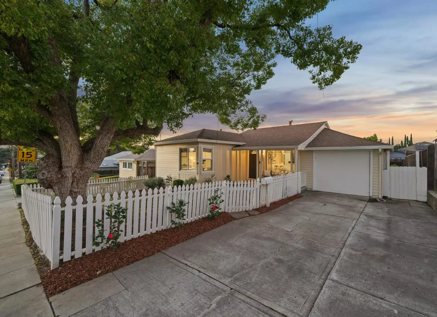 Single-story home with white picket fence, driveway and attached garage at dusk